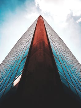 Striking low angle view of a modern skyscraper with reflective glass windows against a blue sky.
